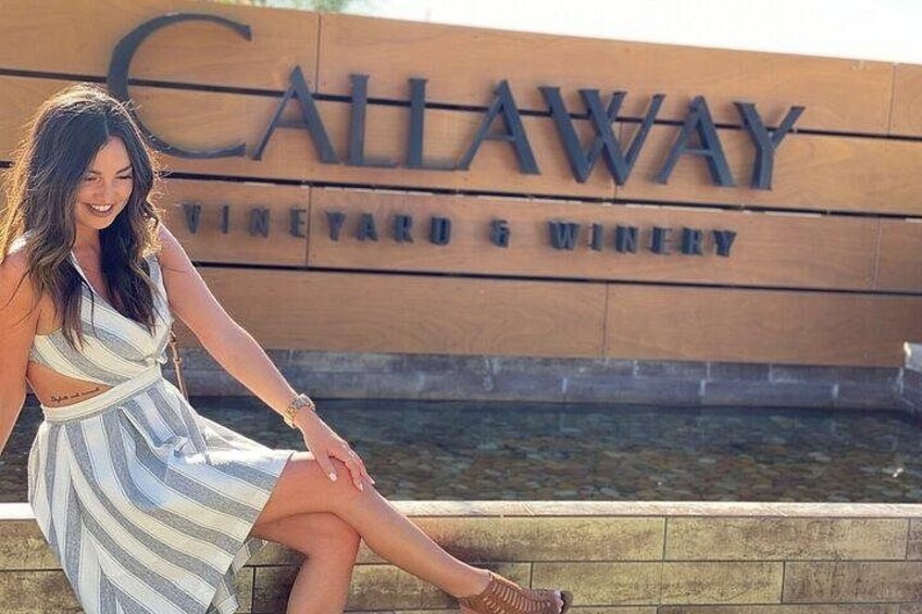 A woman sitting by a sign for Callaway Vineyard & Winery. 5