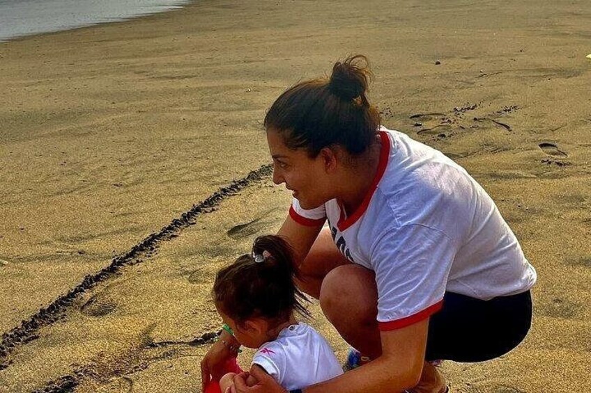 A woman and a child on a sandy beach, with footprints and a tire track visible. 3