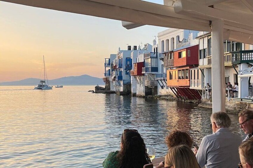 Scena con edifici sul lungomare, una barca a vela e persone che cenano. 2