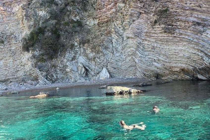 A clear turquoise sea, rocky cliffs, and a person swimming. 4