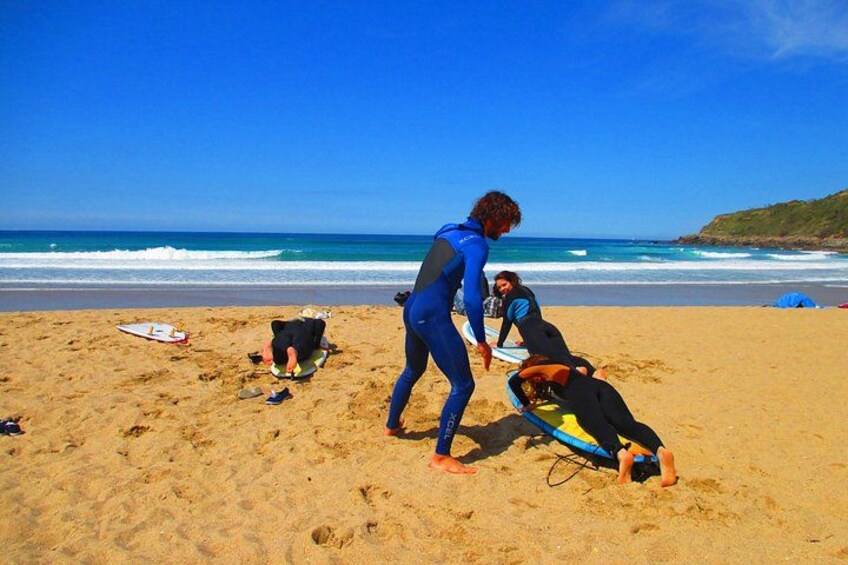 A beach with people in wetsuits, a surfboard, and a person lying on a mat. 2