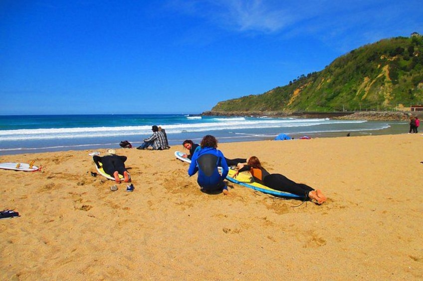 A beach with people lying on surfboards, a sandy shore, and a hilly coastline. 1