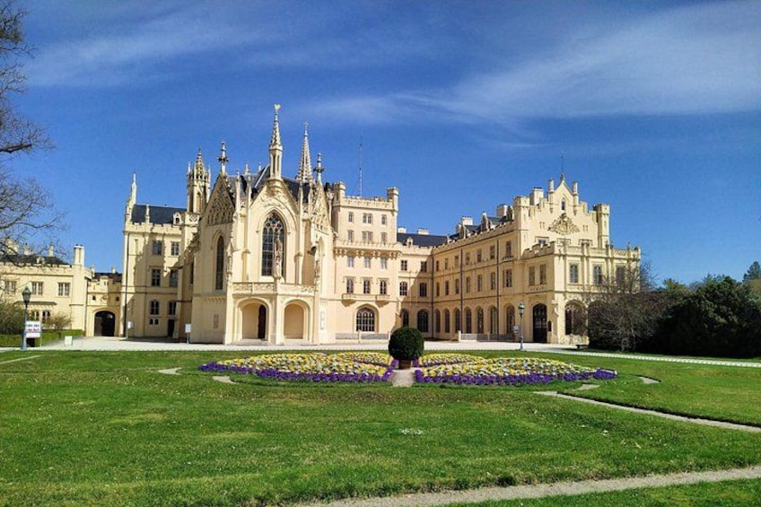 A large, ornate building with a symmetrical facade, surrounded by a well-maintained lawn and flower beds. 1