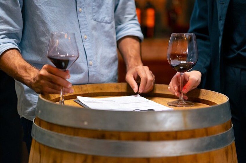 Une personne tenant un verre de vin près d’une barrique en bois. 4