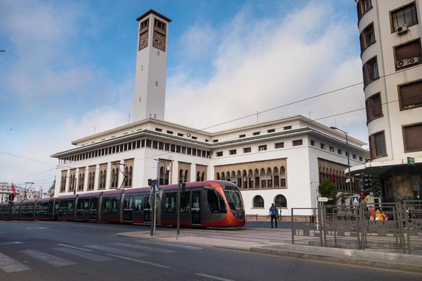 A train station with a clock tower, a red train, and a modern building. 2