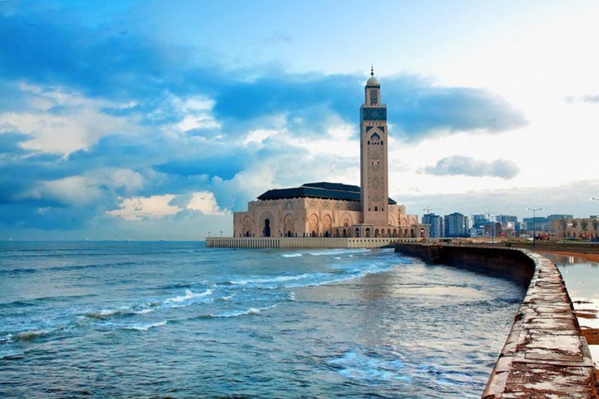A coastal building with a tower, a pier, and a city skyline in the background. 1