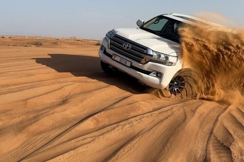 Ein weißer Toyota Land Cruiser fährt durch eine Wüstenlandschaft mit Sanddünen. 1