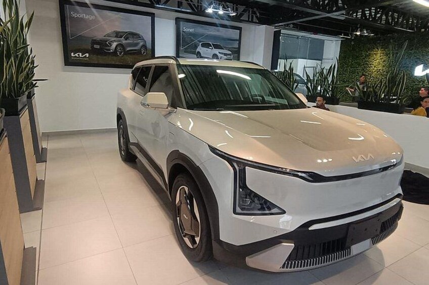 En hvid Kia Sportage SUV i et udstillingslokale med flisegulv og indendørs planter. 4