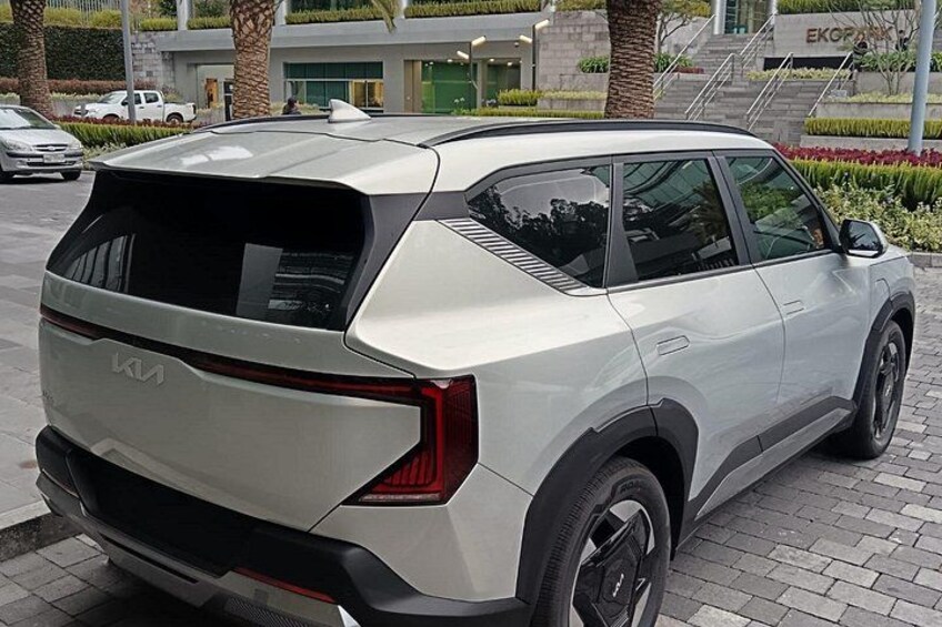 En hvid SUV parkeret på en belagt plads med en bygning og palmer i baggrunden. 5