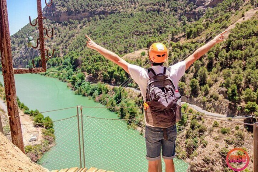 A person standing on a bridge with arms outstretched, overlooking a river and a mountainous landscape. 3