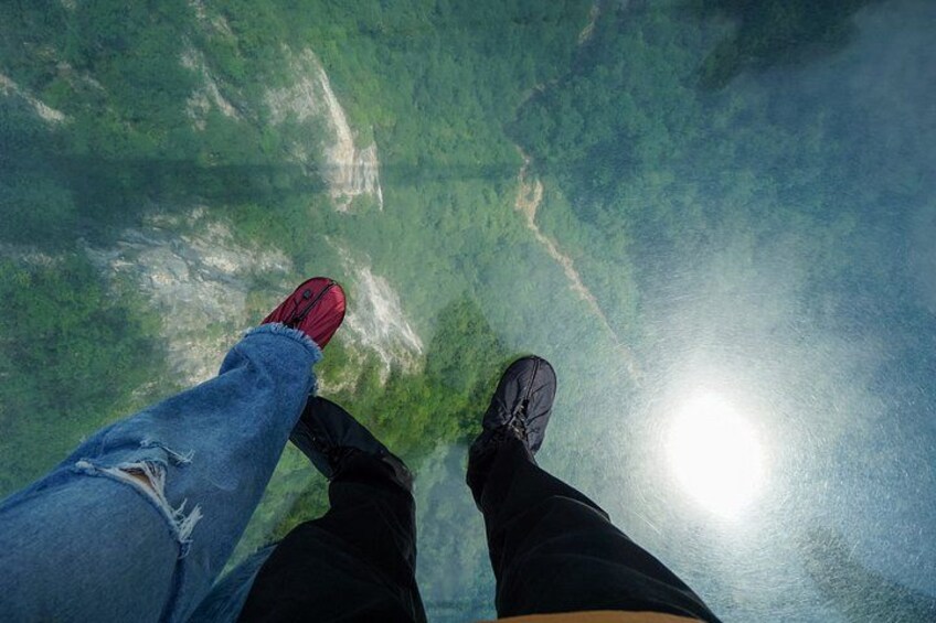 Beine einer Person in roten und schwarzen Schuhen, stehend auf einer spiegelnden Fläche vor einer grünen Landschaft. 2