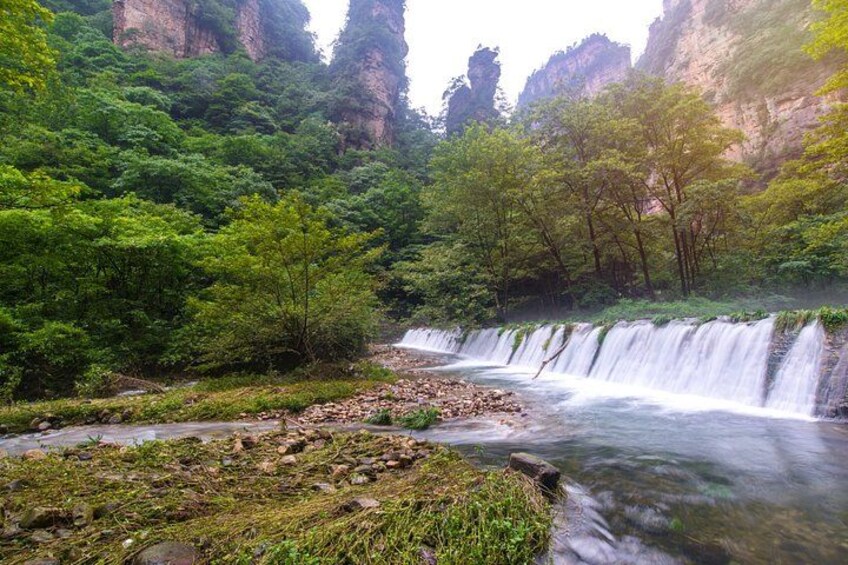 A waterfall in a lush green valley with rocky terrain and dense foliage. 3