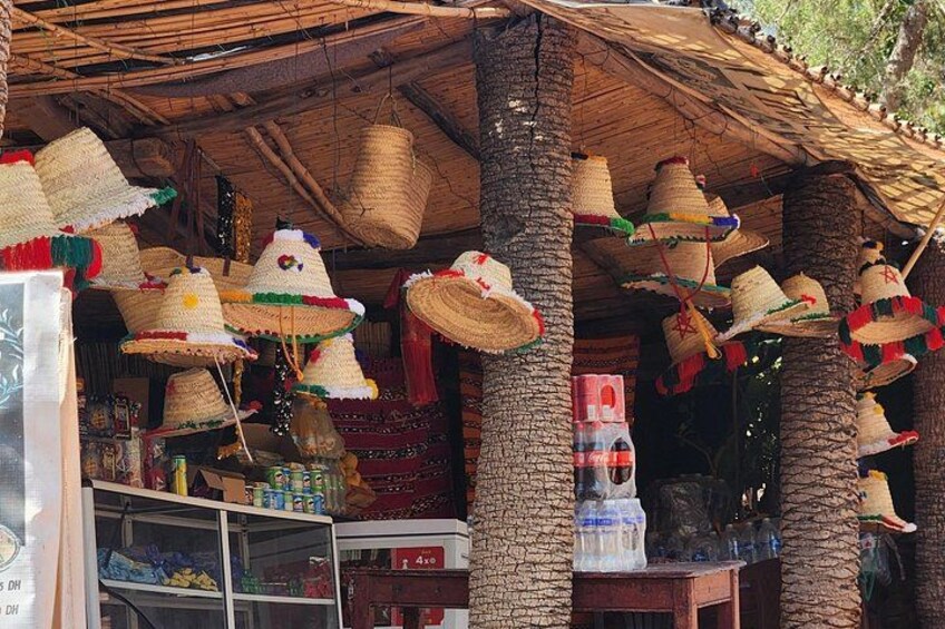 A market stall with woven hats hanging from the ceiling and various items on display. 2