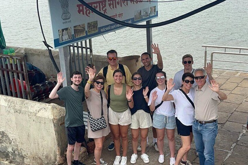 A group of people posing in front of a signboard with text and a railing. 3