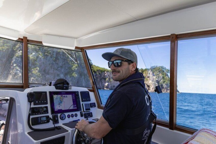 A man steering a boat with a control panel and a view of the sea and cliffs. 4