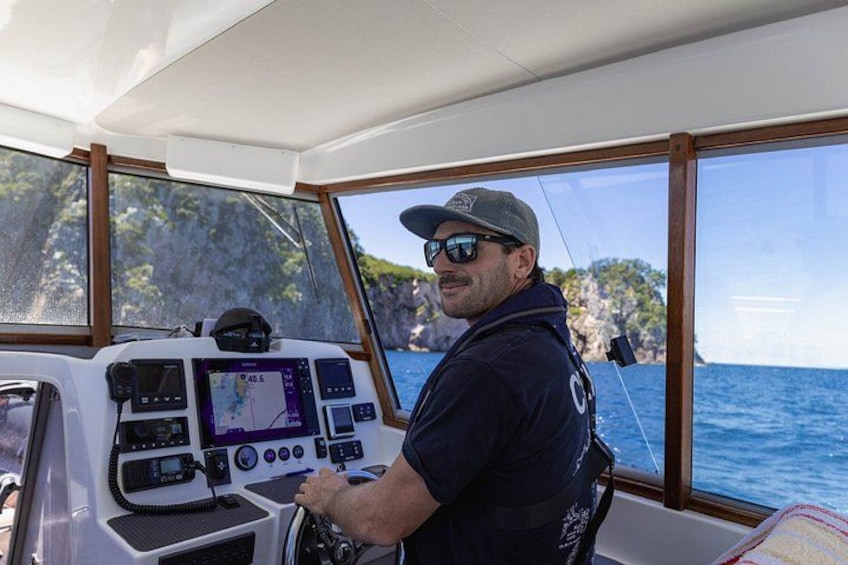 Un hombre maneja una embarcación con un panel de control, con vista al mar y acantilados. 5