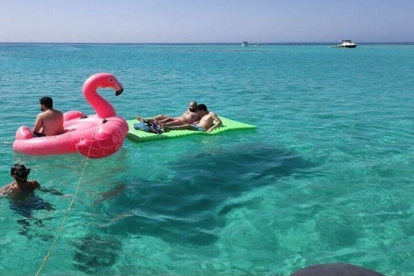 People floating on a turquoise sea, a pink flamingo float, and a green raft. 1