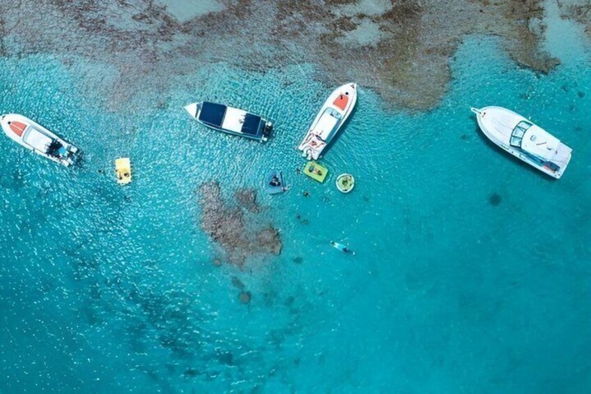A turquoise sea with several boats anchored, including a white yacht and a smaller motorboat. 3