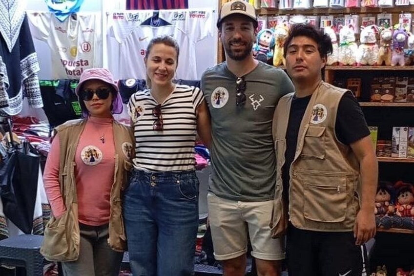 Vier personen staan in een winkel met rekken vol kleding en speelgoed. 4