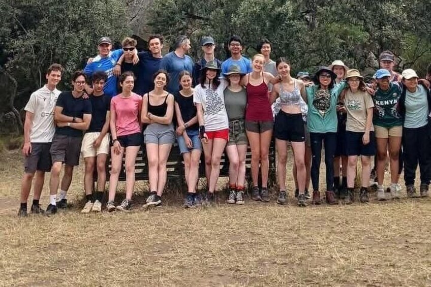 A group of people standing outdoors in a dry grassy area with trees in the background. 4