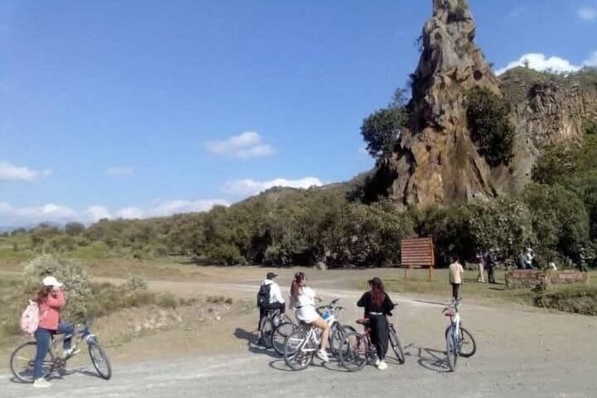 A group of cyclists on a paved path with a large rock formation in the background. 2