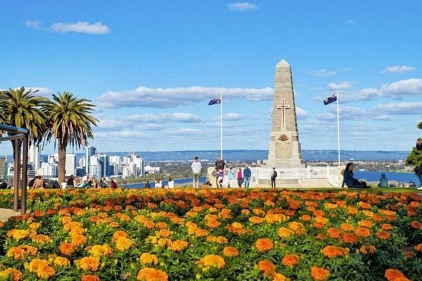 A monument with a cross, surrounded by marigold flowers, palm trees, and a city skyline in the background. 4