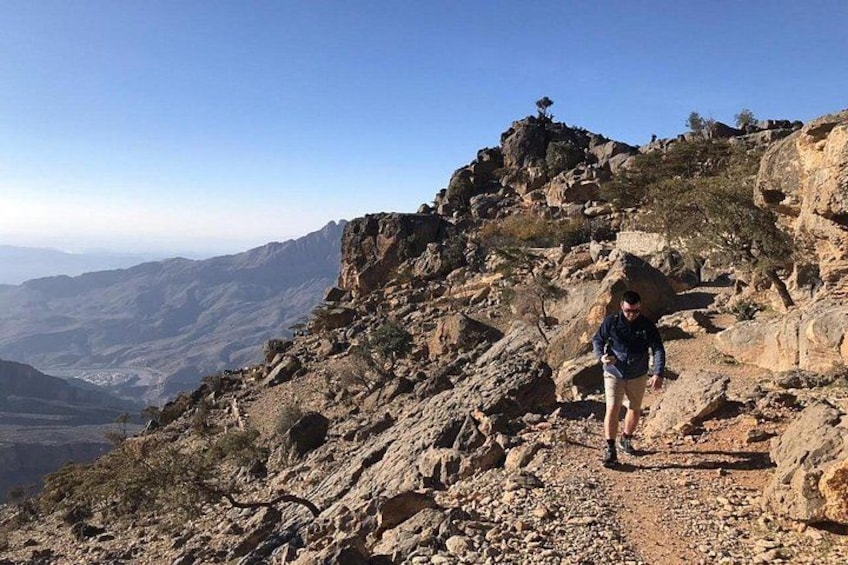A hiker on a rocky mountain trail with a view of distant valleys and a clear sky. 3