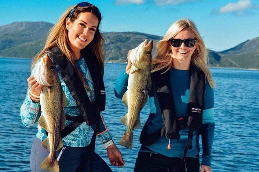 Two people holding fish on a boat with a lake and mountains in the background. 3