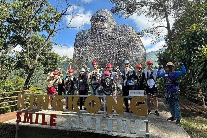 Un groupe de personnes posant devant une grande sculpture aux textures variées, sur laquelle on peut lire les mots « ENGKONG » et « ZONE DE SOURIRE » sur une pancarte. 3