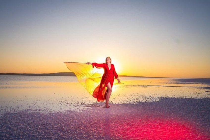 A person in a red dress with a yellow wing-like accessory on a beach at sunset. 4