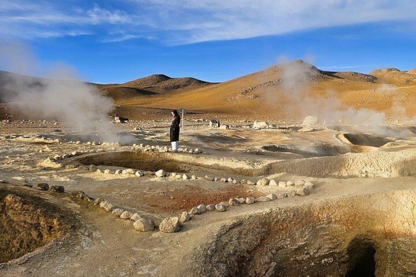 A geothermal area with steam vents, a person standing, and a rocky terrain. 4