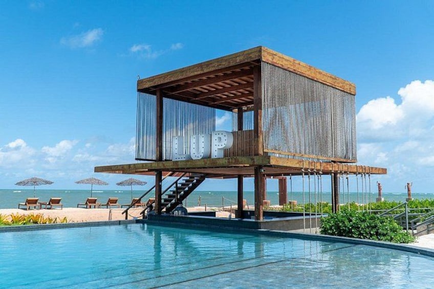 A wooden structure with a pool, surrounded by beach chairs and umbrellas. 3