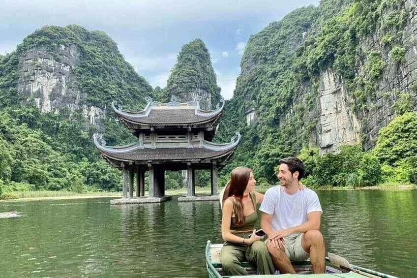 A couple on a boat near a traditional Chinese pavilion by a river surrounded by cliffs. 1