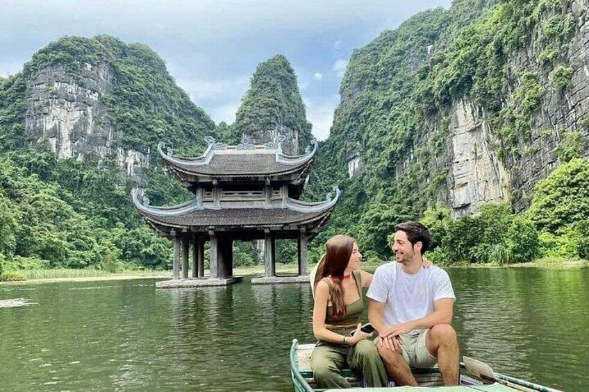 A couple on a boat near a traditional Chinese pavilion by a river with cliffs in the background. 3