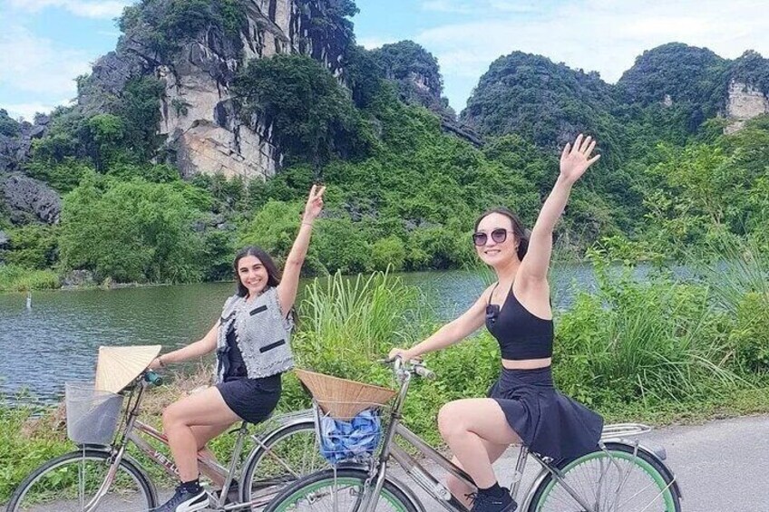 Two people on bicycles by a river with greenery and cliffs in the background. 5