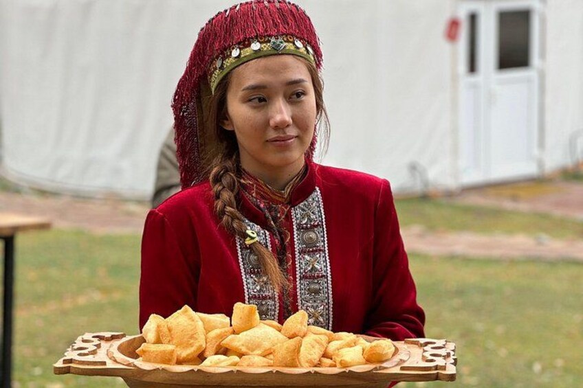 Eine Person in traditioneller Kleidung hält ein Tablett mit Essen. 3