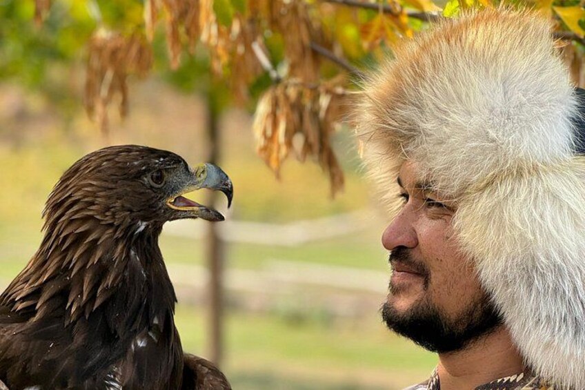 Eine Person mit Fellhut und Vogel, vermutlich ein Adler, in einer natürlichen Umgebung mit Bäumen. 2