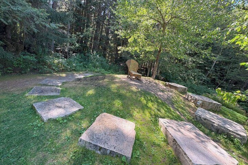 A stone bench in a forested area with a stone pathway leading to it. 2