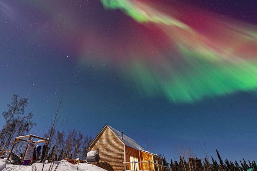 A wooden cabin with a snow-covered roof, a clear night sky, and the aurora borealis. 2