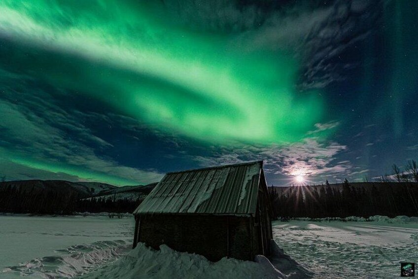 A wooden cabin in a snowy landscape with the Northern Lights in the sky. 1