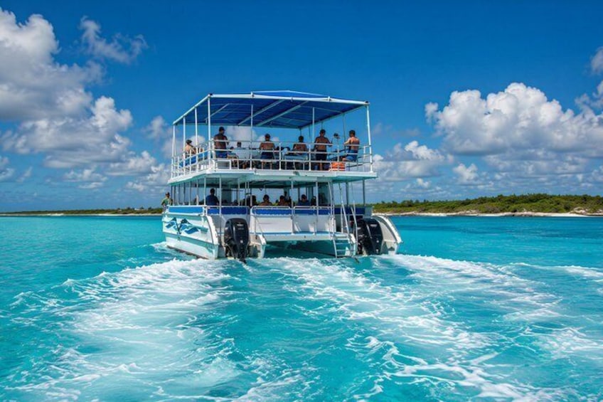 A multi-deck boat with passengers on a clear turquoise sea. 1