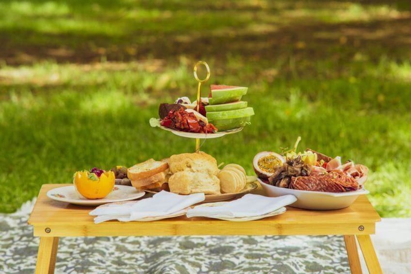 A picnic setup with a fruit platter, bread, and a bowl of snacks on a wooden table. 3