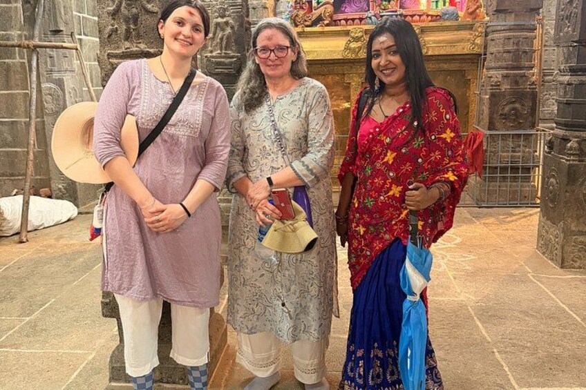 Drie personen staan voor een tempel met stenen beeldhouwwerken en een gouden standbeeld. 1