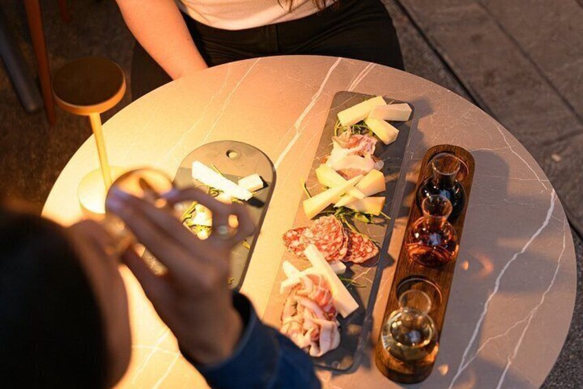 A table with various cheeses, meats, and a bottle of wine. 1