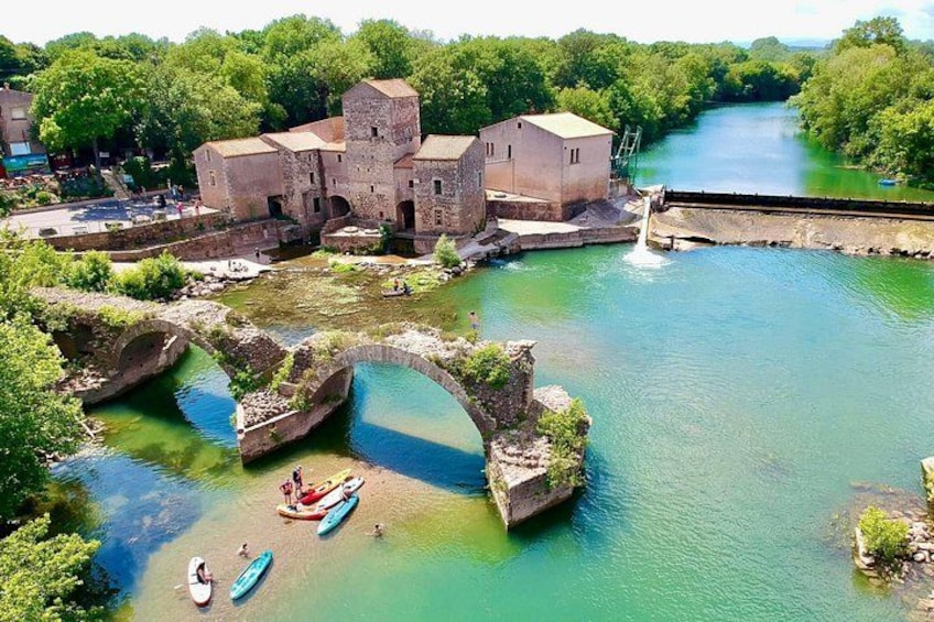 A historic stone bridge over a river, surrounded by lush greenery and a castle-like structure. 1