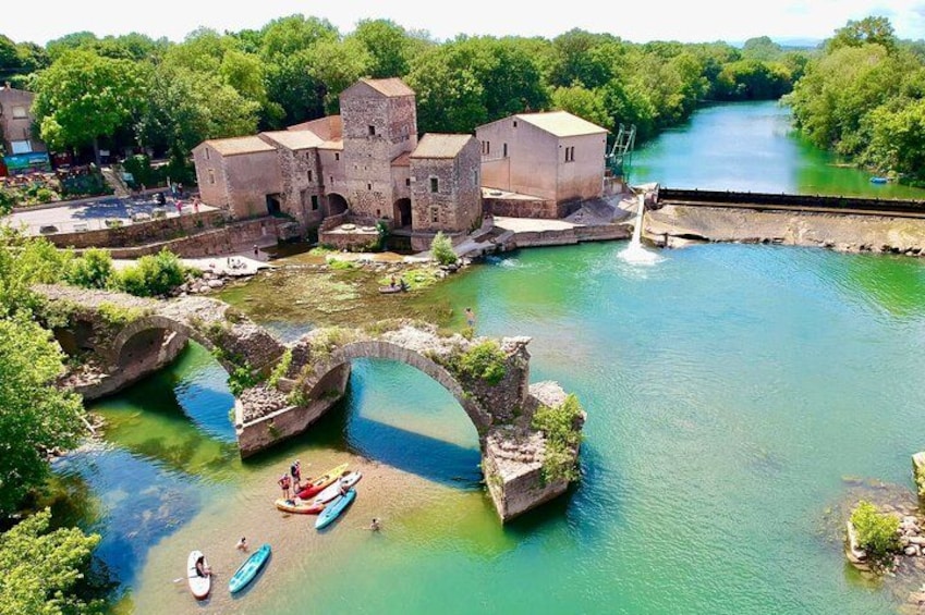 A historic building complex with a river, a stone bridge, and canoes. 1