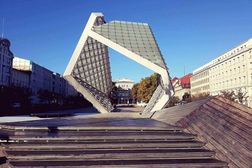 A modern architectural structure with a tilted design, surrounded by traditional buildings and a clear sky. 4