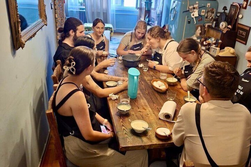 A group of people sitting around a wooden table in a kitchen, engaged in a meal. 4