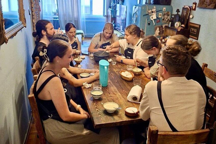 A group of people sitting around a wooden table in a room with blue walls and a window. 2
