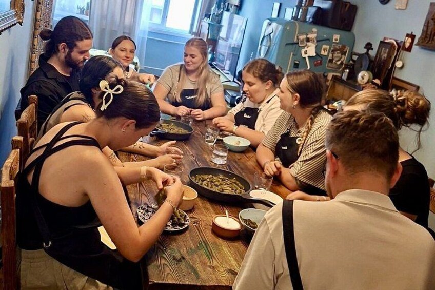 A group of people dining at a wooden table with various dishes and a pan. 5